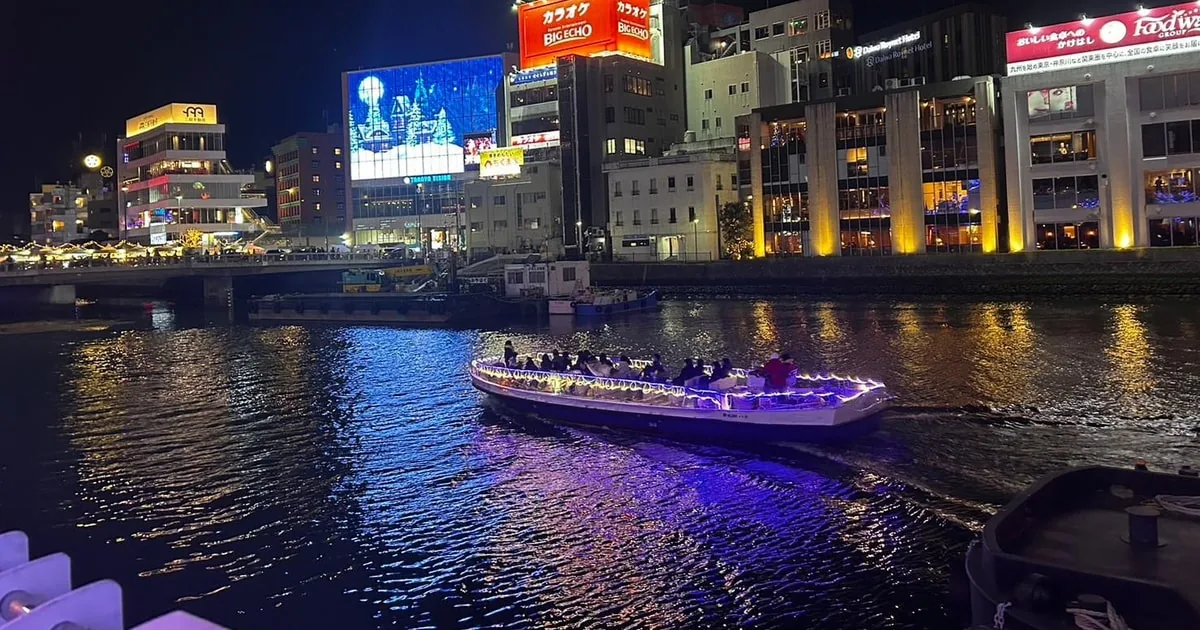 Nakasu bei Nacht: ein beleuchtetes Ausflugsboot auf dem Fluss vor neonbeleuchteten Gebäuden