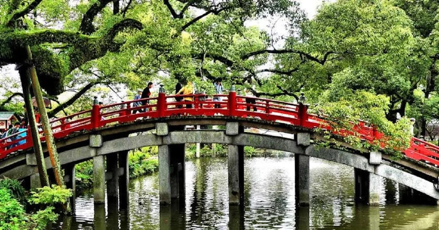 Eine rote Bogenbrücke über einem Teich unter alten Kampferbäumen am Dazaifu-Tenmangu-Schrein