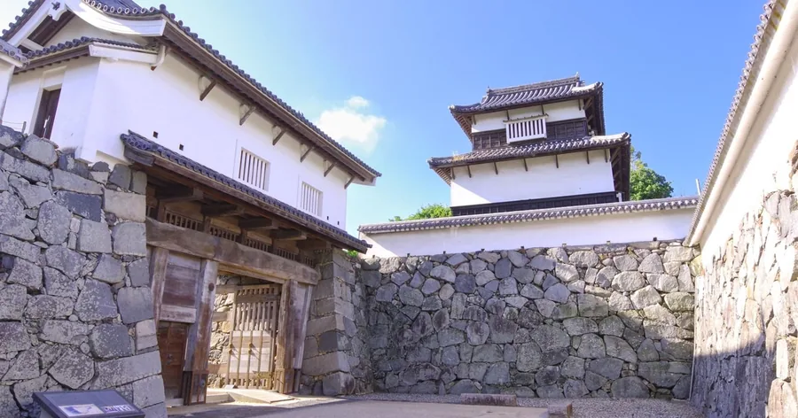 Steinmauern und ein weißer Wachturm an der Burgruine Fukuoka unter blauem Himmel