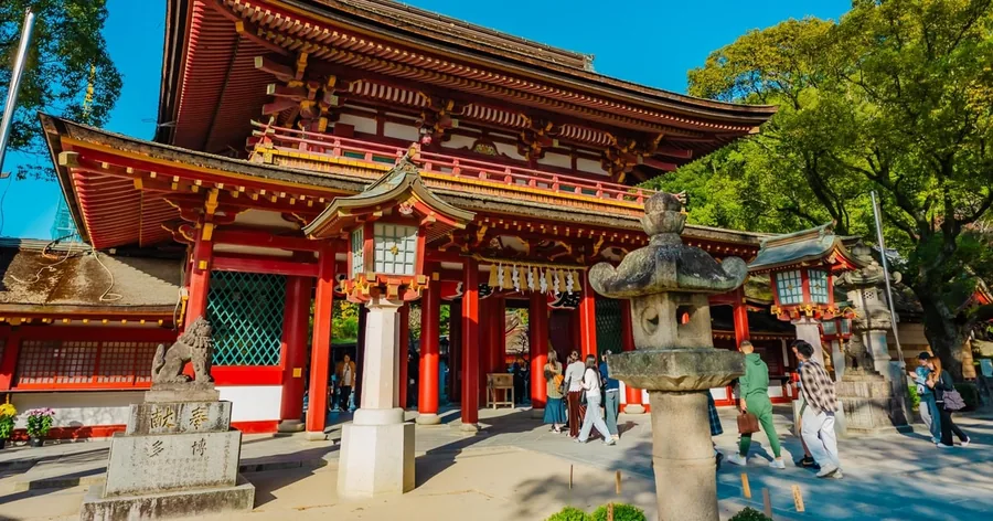 Das rote zweistöckige Tor des Dazaifu-Tenmangu-Schreins mit Steinlaternen und Besuchern im Hof