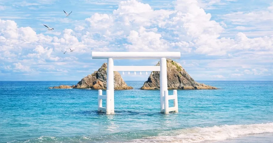 Ein weißes Torii im türkisfarbenen Meer vor den beiden Meoto-Iwa-Felsen bei Itoshima