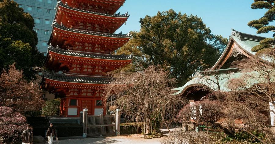 Eine kleine Gruppe geht durch eine Gasse in der Altstadt von Hakata auf die rote fünfstöckige Pagode des Tochoji zu